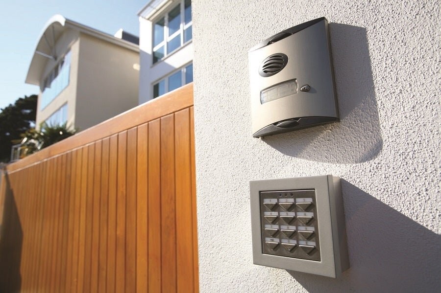 A home’s exterior showing a smart security alarm and wall pad with the home in the background.