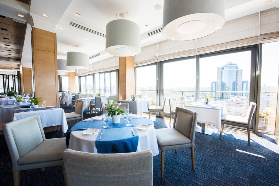  Image is of a beautiful modern restaurant with blue tablecloths and white lighting fixtures on the ceiling. 