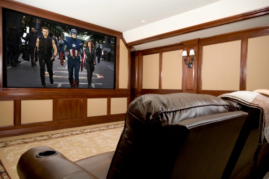 Home theater room with reclining chairs and a large screen showing a superhero movie scene.